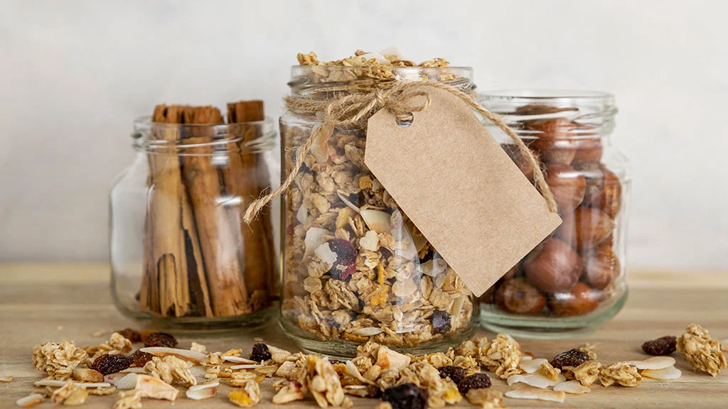 Frascos de vidrio con granola, canela y frutos secos con etiqueta para etiquetado de alimentos.