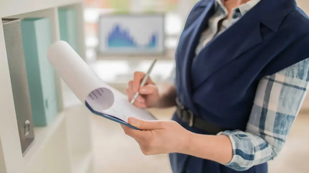 Mujer revisando y firmando documentos en una oficina administrativa.